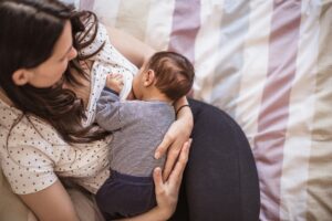A mother lovingly breastfeeding her baby while sitting on a bed in a cozy bedroom setting