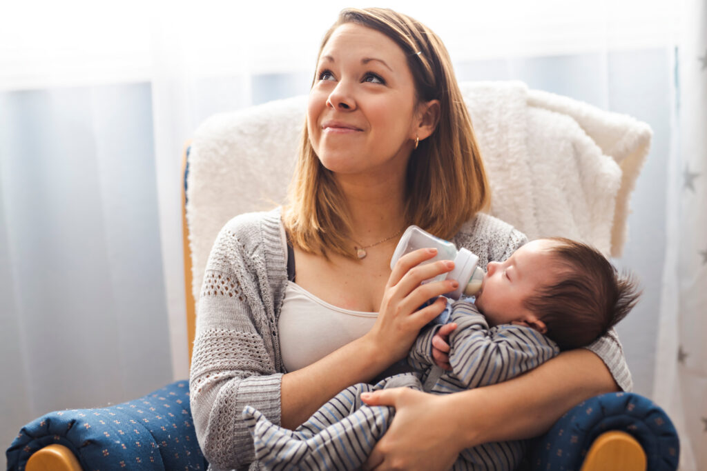 mother feeding her newborn baby from a bottle while relaxing at home